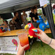 Katniss trinkt einen Cocktail Das Stofftier der Fachschaft - ein roter Papagei - trinkt aus einem orangenen Cocktail. Im Hintergrund ist der Cocktailstand der Fachschaft zu erkennen.
