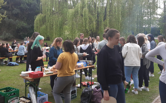 Mitten im Grünen (auf der Wiese vor der EF50) stehen viele Menschen um einen Grill. Das kann nur bedeuten, dass die Fachschaft ihr berühmtes Fachschafts- bzw. Fakultätsgrillen veranstaltet. Bei Bier und Softgetränken, sowie allerlei leckerer Nahrungsmittel sind die Studierenden sitzend oder stehend in Gespräche vertieft.